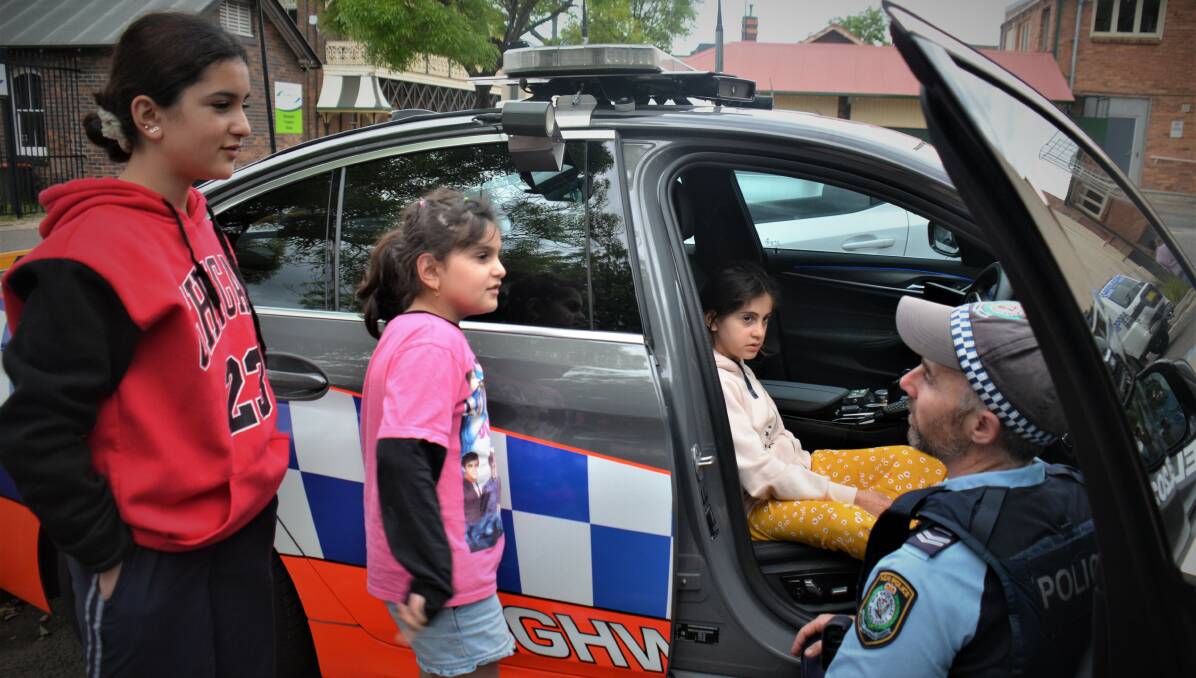 Senior Constable Christopher Belson shows Ezidi children in Armidale how a cop car works, sirens and all. Picture by Rachel GRAY