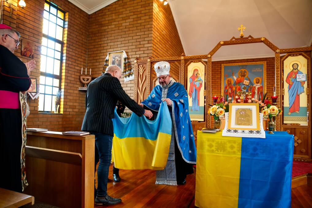 SUPPORT FROM AFAR: A prayer service for Ukraine at St Volodymyr Ukrainian Catholic Church in Wollongong on Saturday, with Father Simon Ckuj presenting a Ukrainian flag to Wollongong Lord Mayor Gordon Bardbery. Picture: Anna Warr