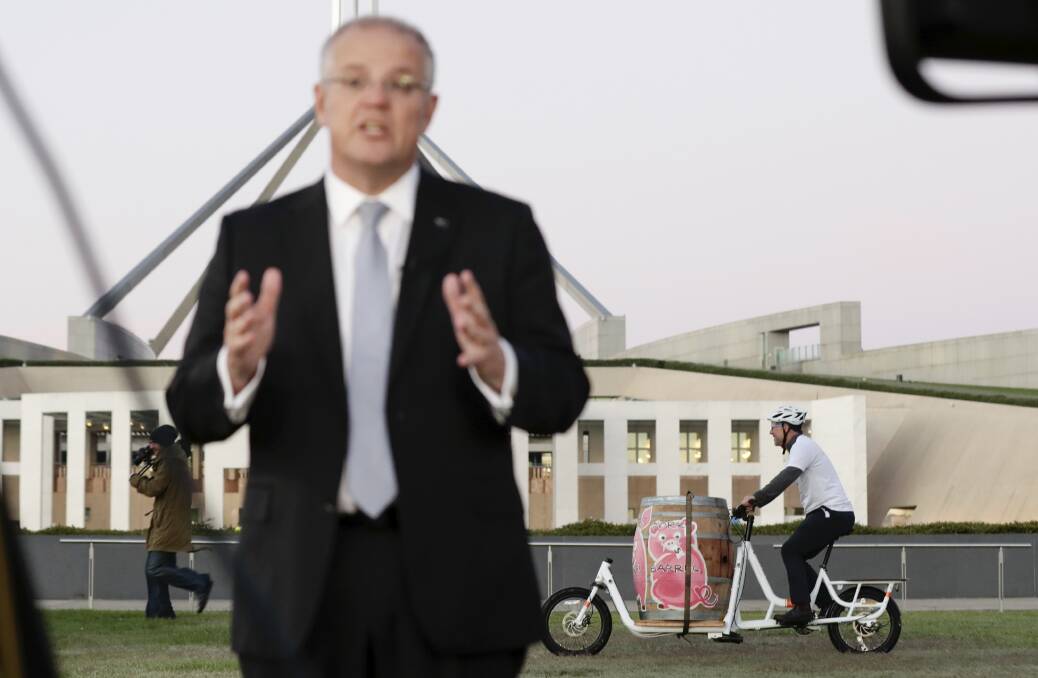 A man wheels around a pork barrel as Prime Minister Scott Morrison does a Budget-sell interview on breakfast television on the front lawn of Parliament House in Canberra on Wednesday. Photo: Alex Ellinghausen