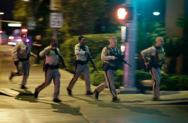 Police run to cover at the scene of a shooting near the Mandalay Bay resort and casino on the Las Vegas Strip, Sunday, Oct. 1, 2017, in Las Vegas. Multiple victims were being transported to hospitals after a shooting late Sunday at a music festival on the Las Vegas Strip. (AP Photo/John Locher)