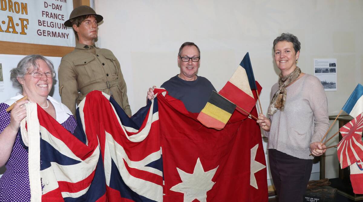 EXHIBITION: Armidale Folk Museum staff Bronwyn Clarke (left), Ivan Thornton and Hayley Ward hold an Australian Red Ensign and allied flags used by local citizens to celebrate the end of World War I.